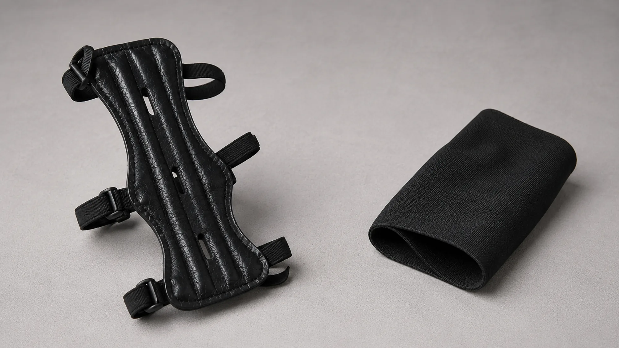 The rigid three-strap arm guard beside a plain black elastic archery sleeve half rolled to show it is fabric only